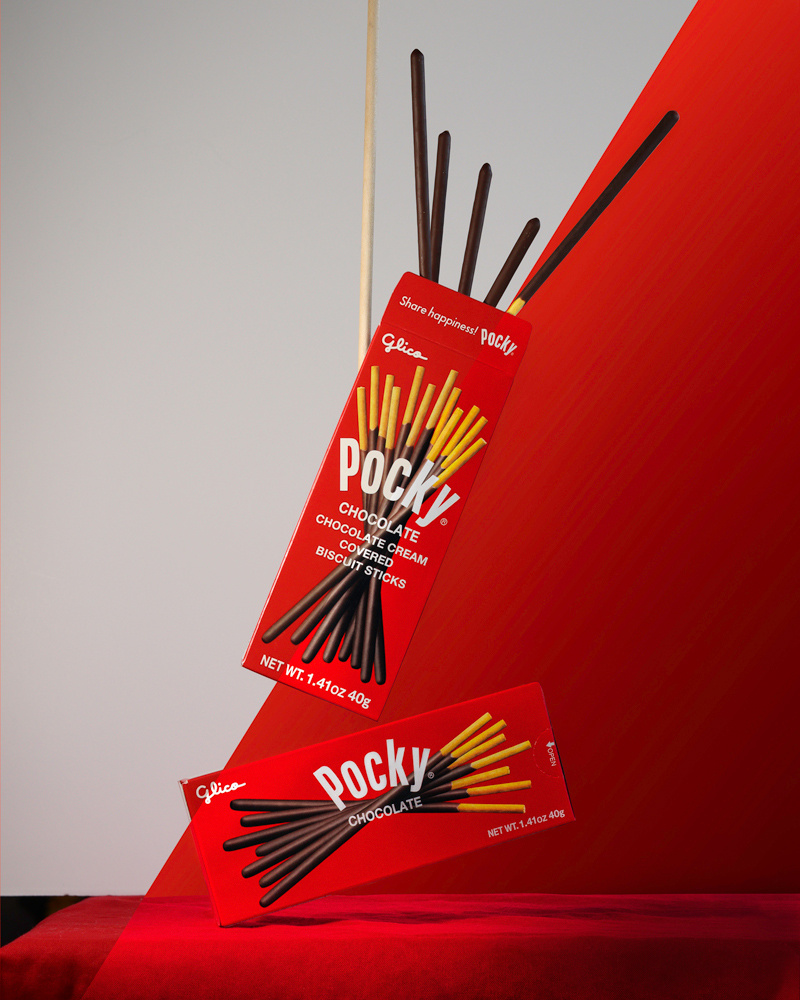 Digital retouching and editing. 2 photos merged together of a before and after of 2 hovering pocky boxes on a red background.